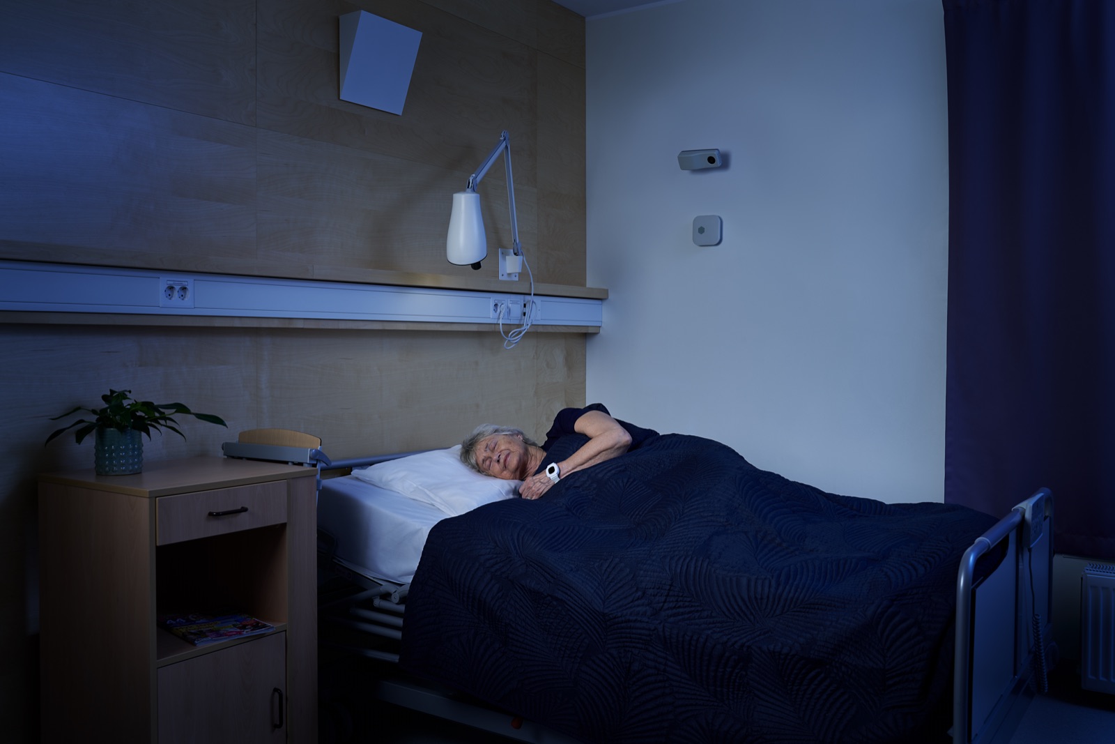 Eldre kvinne sover om natten med digital tilsynssensor på veggen